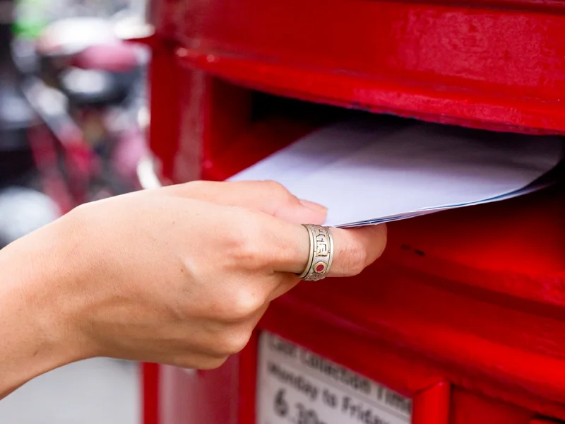 Close up of a hand posting letters into a red postbox