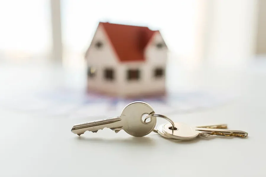 Close up of a set of house keys. A model house can be seen in the background.