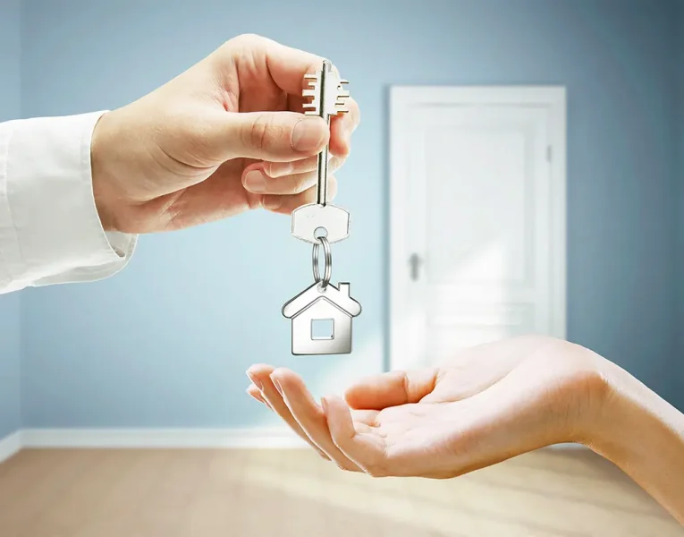 A man drops a house key attached to a house-shaped key ring into a woman's outstretched hand.