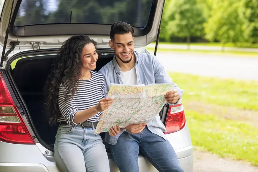 A young couple examine a paper road map as they prepare for a romantic road trip.