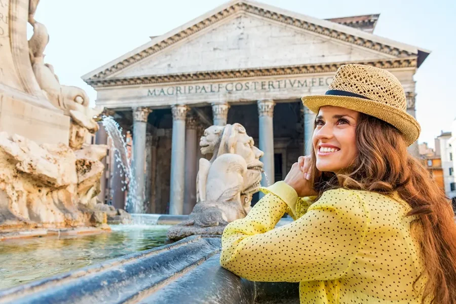 A smiling woman standing by a fountain in front of the Pantheon in Rome, Italy.
