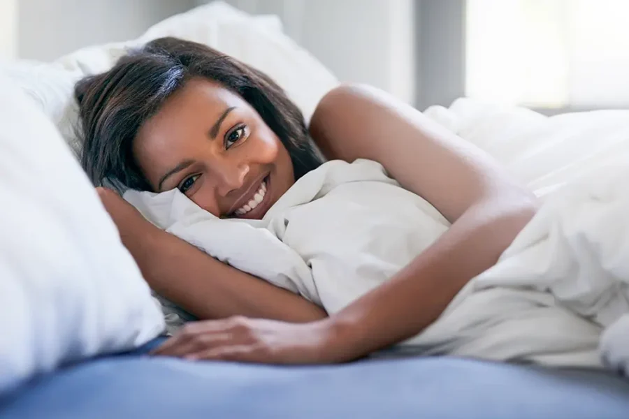 A woman lying in bed, smiling after a good night's sleep.