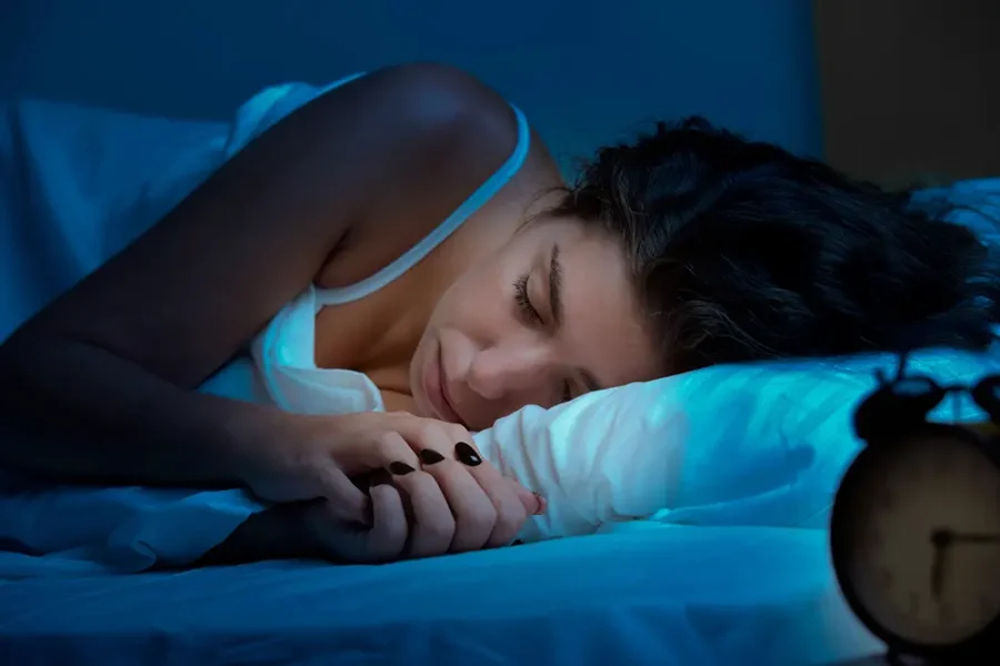 A woman sleeping in a hotel bed. Blue light falls on her through the window.