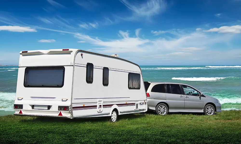 A car and caravan parked on grass overlooking the sea.