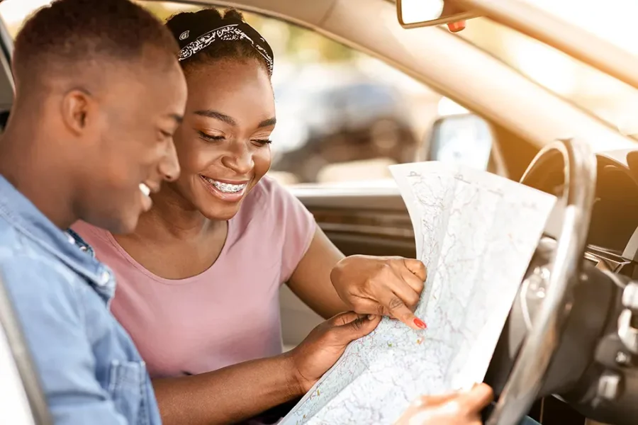 A young Black couple smile as they plan their route for a road trip.